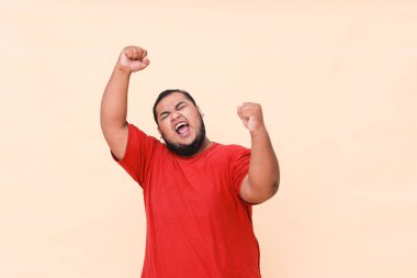 Mutlu ve gülümseyen Asyalı genç adam başarı ve başarıyı kutlamak için kolunu kaldırıyor..