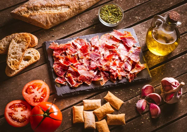 Kahverengi ahşap bir masanın üzerindeki tahta tabaktaki İberya jambonu. Etrafında bazı malzemeler var. Tipik İspanyol yemekleri. Domuz eti..