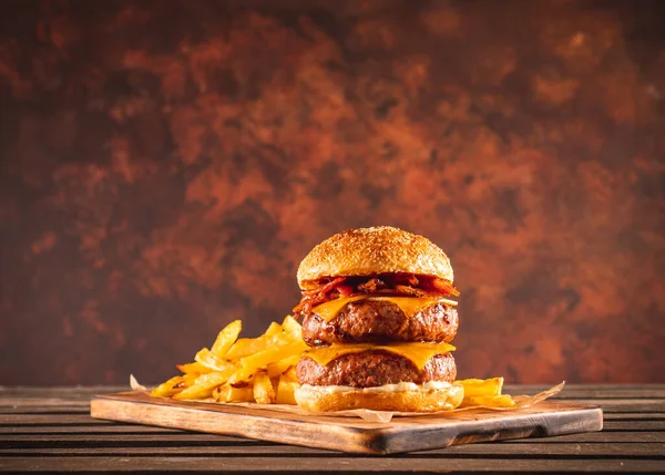 Duble sığır eti ve pastırmalı burger. Çedar peyniri ve patates cipsi. Masadaki tahta tahta üzerinde, yemeye hazır. Boyut XL.