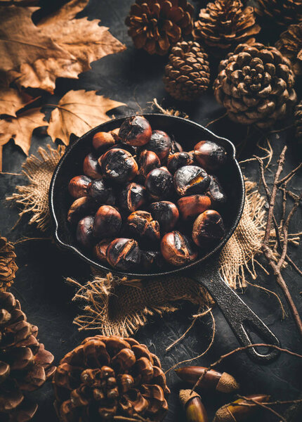 Roasted chestnuts in a small iron pan on a table with autumn leaves and pine cones. Ready to eat. Traditional autumn food.
