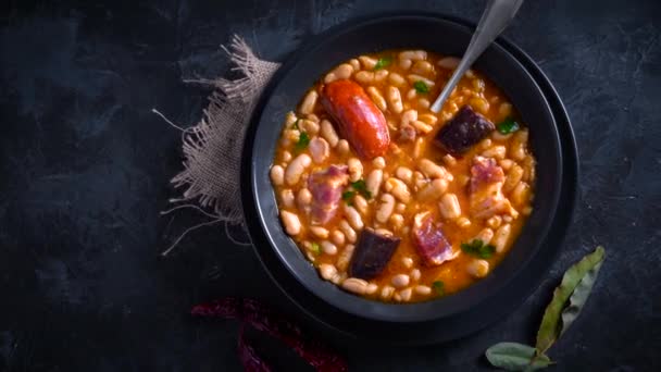 传统的豆子配方 配上辣椒酱和血香肠 叫做法贝达阿斯图里亚斯 放在深色桌子上 周围放着一些配料 有伴儿的典型西班牙食物 — 图库视频影像