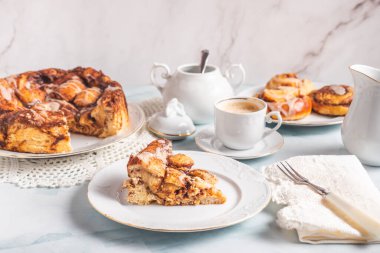 Kahvaltıda kahve ve hamur işi çöreklerle beyaz bir masada beyaz bir tabakta ev yapımı tarçınlı rulo. Geleneksel İsveççe ve Danimarka tarifi.