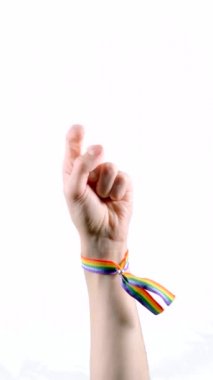 LGBT bayrağı renginde bir bilezik takan el bir parmağını kaldırıyor. Bir şeyi işaret etmek ya da sırasını beklemek. LGBT sembolü. Dikey video.