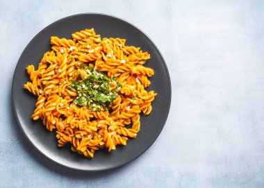 Masadaki yuvarlak siyah tabakta domates ve gremolata soslu kıvırcık makarna. Yemek hazır..