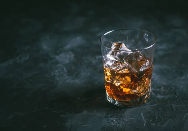Glass of whiskey with ice on a dark table. Alcoholic beverage ready to drink. Photo with copy space. 