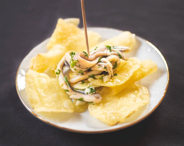 Potato chips with pickled anchovies in a white round plate on a table. Typical Spanish food called tapa to eat in a bar.