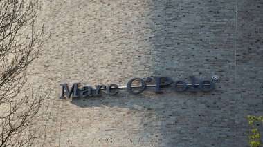 Metzingen, Almanya - Mai 03, 2021: Bir tuğla dış cephede siyah Marco direk harfleri. Ön planda kahverengi ve yeşil dallar.