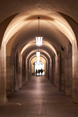 Gece bir bina bulvarında şehir feneri. Yuvarlak kasa ve sütunları olan bir mimari. Derinlik bulanıklığında 3 kişi.