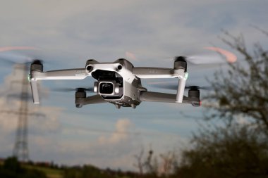 Nurtingen, Germany - June 26, 2021: Drone air 2s from the dji company hovers in the air. Electricity pylon and bare tree in front of a blue cloudy sky. Low angle view. clipart