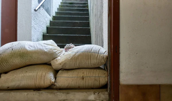 Protective measure against floods in basements. Barrier made of sandbags lies in the entrance area of a residential building. Deep perspective.