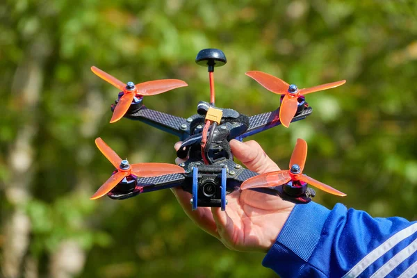 Nuertingen, Almanya - 16 Mayıs 2020: Siyah İHA da turuncu pervaneli dörtlü yarışıyor ve insan eliyle tutuluyor. Arka planda bulanık çimenler. 