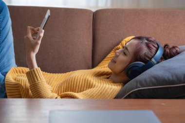 Rahatla, stres at, tatil yap, mutlu, Asyalı kadın evde rahatla akıllı telefondan ve bilgisayardan mutlu bir şekilde müzik dinle..