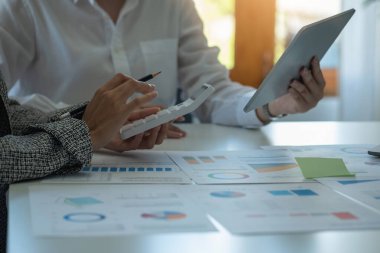 İş kadınları, pazarlama stratejileri planlamak ve şirket için kârlı yatırımlar yapmak için hesap makineleri ve grafik analizi bilgisayar tabletleri kullanır..