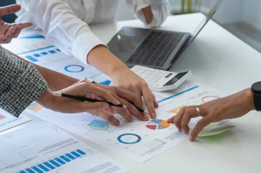 Bir grup işadamı, kazançları için dizüstü bilgisayarları ve grafik çizelgeleriyle plan yapar ve şirketlerinin yıllık bakiyesini hesaplamak için bir hesap makinesi kullanır..