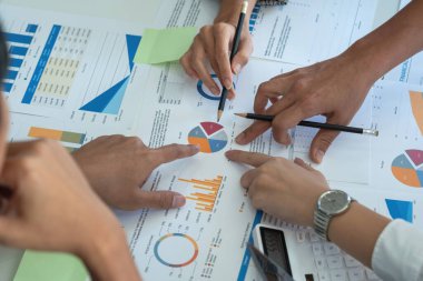 Bir grup işadamı, kazançları için dizüstü bilgisayarları ve grafik çizelgeleriyle plan yapar ve şirketlerinin yıllık bakiyesini hesaplamak için bir hesap makinesi kullanır..