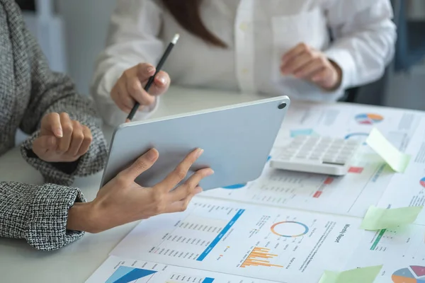 İş kadınları, pazarlama stratejileri planlamak ve şirket için kârlı yatırımlar yapmak için hesap makineleri ve grafik analizi bilgisayar tabletleri kullanır..