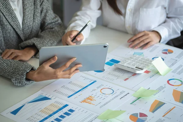 İş kadınları, pazarlama stratejileri planlamak ve şirket için kârlı yatırımlar yapmak için hesap makineleri ve grafik analizi bilgisayar tabletleri kullanır..