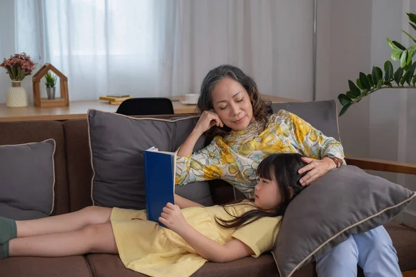 Portrait of an elderly woman and granddaughter reading a book to enhance reading skills and family activities.