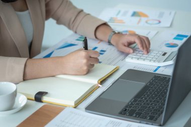 Closeup Portrait of a female accountant using a calculator and laptop to calculate balance using graphs for customers.
