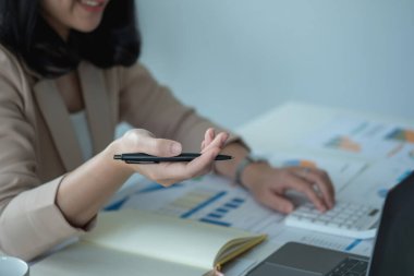 Müşteriler için grafikler kullanarak dengeyi hesaplamak için hesap makinesi ve laptop kullanan bir kadın muhasebecinin yakın plan portresi.