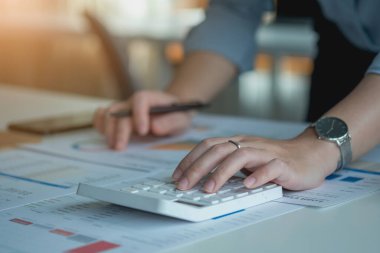 Müşteriler için grafikler kullanarak dengeyi hesaplamak için hesap makinesi ve laptop kullanan bir kadın muhasebecinin portresi.