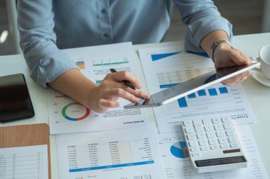 Business women use tablets and calculators and graph analysis to plan marketing strategies and make profitable investments for the company.