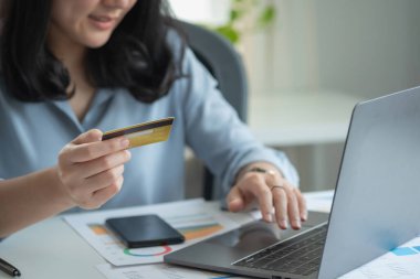 A woman uses a credit card to make online purchases on her laptop. credit card spending concept