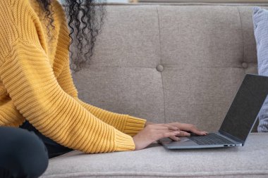 Afro-Amerikalı bir kadın evinde rahatlamak için laptop, akıllı telefon, tablet ve müzik kulaklığı kullanıyor..