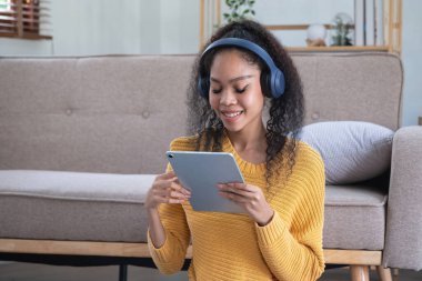 Afro-Amerikalı bir kadın evinde rahatlamak için laptop, akıllı telefon, tablet ve müzik kulaklığı kullanıyor..