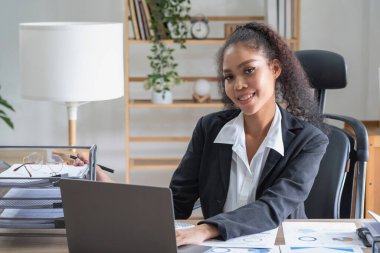 Ofiste çalışan Afrikalı Amerikalı iş kadını laptoplar, grafikler ve ofis ekipmanları kullanıyor..