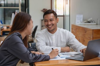 İki erkek ve kadın pazarlamacı şirket karlarını analiz etmek için şirket belgelerini ve dizüstü bilgisayarlarını kullanıyor..