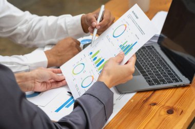 İki erkek ve kadın pazarlamacı şirket karlarını analiz etmek için şirket belgelerini ve dizüstü bilgisayarlarını kullanıyor..