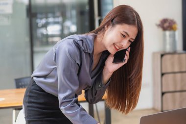 Ofis masası bilgisayarındaki müşterilerle sohbet etmek için cep telefonu kullanan iş kadını kalem hesap makinesi ve belgeler yerleştiriliyor