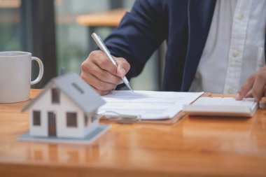 Muhasebeci, iş adamı, emlakçı, iş adamı müşterilere model ev veriyor. Müşterilerin imzalaması için ev faizi hesapları dökümanları da var..