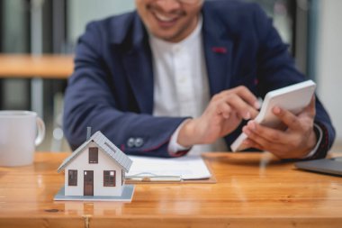Muhasebeci, iş adamı, emlakçı, iş adamı müşterilere model ev veriyor. Müşterilerin imzalaması için ev faizi hesapları dökümanları da var..