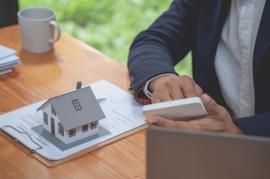 Muhasebeci, iş adamı, emlakçı, iş adamı müşterilere model ev veriyor. Müşterilerin imzalaması için ev faizi hesapları dökümanları da var..