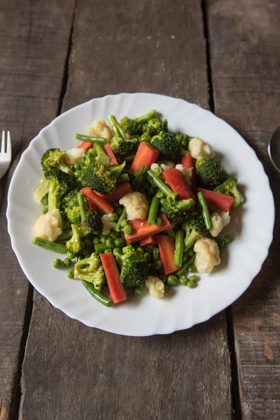 Fresh boiled vegetables saute served in a white plate. Top view.