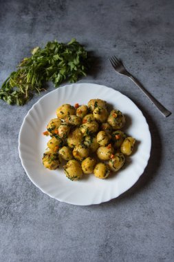 Dum aloo or fried baby potatoes tossed in oil in a white plate. Top view.