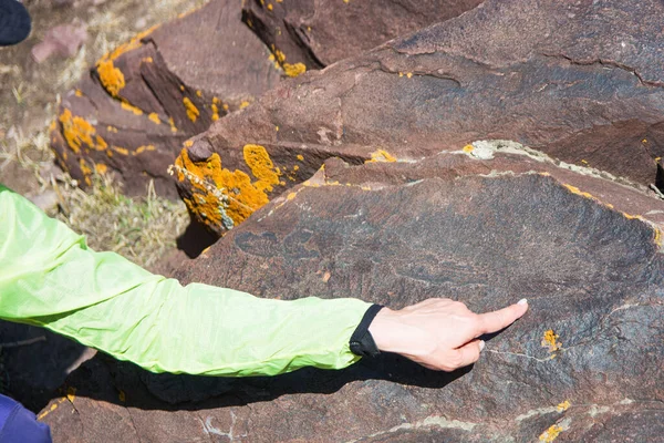 La ragazza da vicino indica i disegni sulla pietra. Antico petroglifo situato a Boom Gorge. — Foto Stock