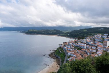 San Roque 'un bakış açısından Lastres' in balıkçı köyü manzarası, arka planda Asturias dağları ve La Griega ve Lastres plajları, bulutlu gökyüzü, dikey