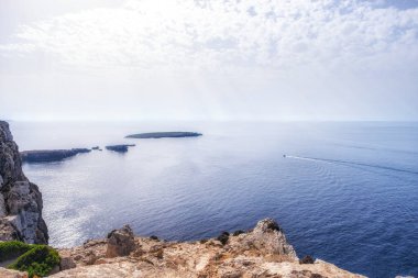 Menorca 'daki Süvari Fenerinden kayalıkların ve Akdeniz' in manzarası. Bir tekne, yaz günü, yatay olarak denizde bir uyanış yapar.