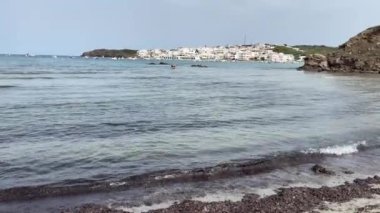 panoramic view of a Mediterranean fishing village with white houses, from a white sandy beach with algae on the shore, village of Es Grau from the cove of En Vidrier, in Menorca, Balearic Islands, Spain