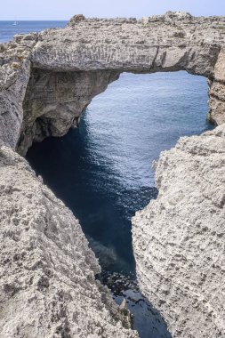 a rocky grotto in a cliff forming a natural bridge or natural bow over the sea, cave named Bufador of Benibequer, in Menorca, Balearic Islands, Spain, vertical