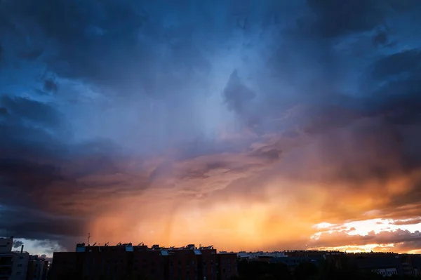 a summer storm at sunset over a city with a sky in shades of orange and blue, contrasting bluish and orange complementary colors in a dramatic sky, cloudscape