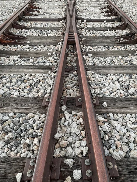 railroad crossing, rusty railroad rails seen from above with wooden sleepers and white gravel around them, vertical