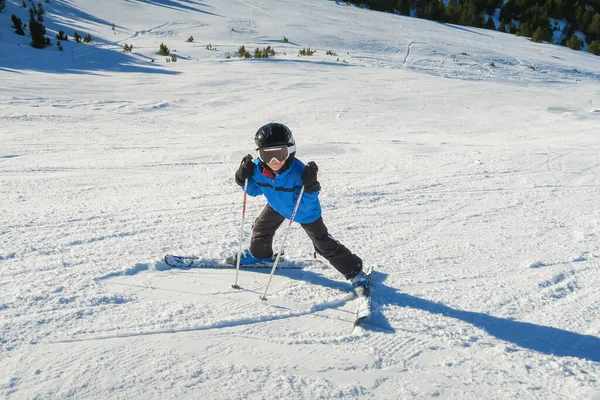 a little beginner skier on a ski slope in a funny inverted position and smiling behind the goggles looking at the camera, child having fun learning to ski, horizontal