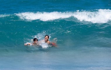 İki genç arkadaş sahilde dalgalarla, büyük dalgalarla, yaz eğlenceleriyle, yatay dalgalarla eğleniyor.