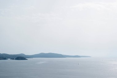 Uçurumların sonsuzlukta kaybolduğu minimalist kıyı şeridi, sakin bir denizde küçük bir yelkenli, Menorca, Balear Adaları, İspanya