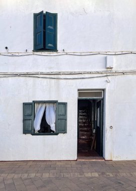 Geleneksel beyaz bir evin ön cephesinde, Akdeniz 'de bir balıkçı köyünde, kapı ve pencereler açık, ve havada hareket eden perdeler, beyazlatılmış, Fornells, Menorca, İspanya