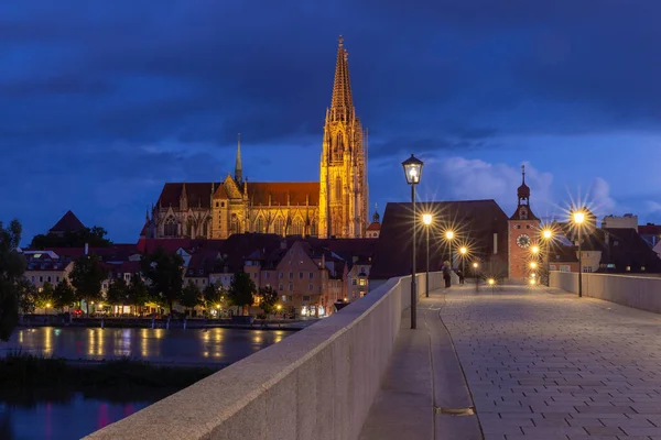 Regensburg. Starý kamenný most přes řeku Dunaj v nočním světle. — Stock fotografie